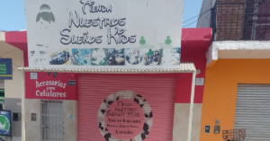 Fachada del local Nuestros Sueños Kids, pintada de blanco y naranja, con cartel artesanal, cortina roja y rubro accesorios para celulares y ropa